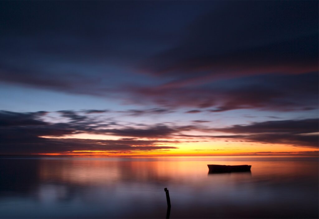 Lone boat on calm sea at twilight with warm evening colors and soft clouds wallpaper background