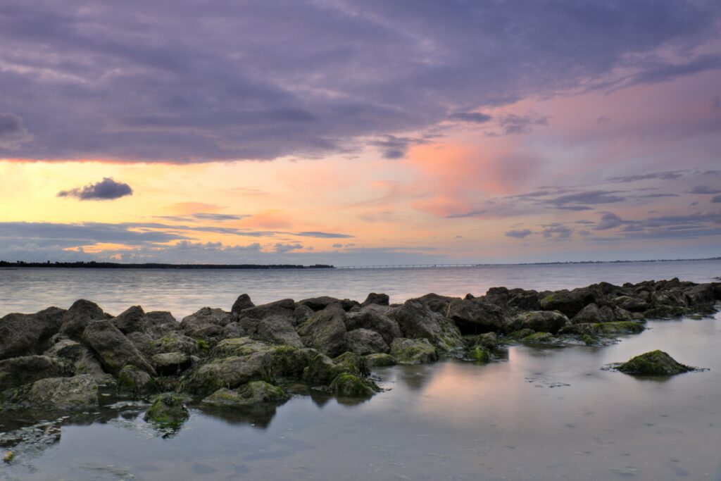 Tranquil seascape wallpaper with calm waves and rugged stones under a colorful twilight sky