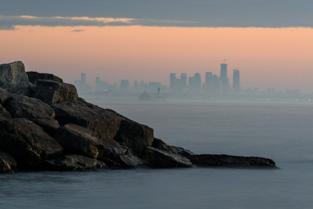 Tranquil twilight seascape with rugged rocks calm water and hazy city skyline pastel sky wallpaper