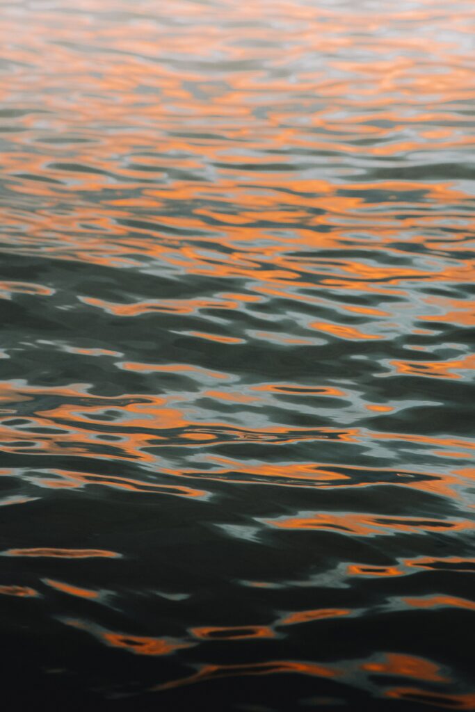 Tranquil water with gentle waves reflecting warm orange and pink hues abstract wallpaper background