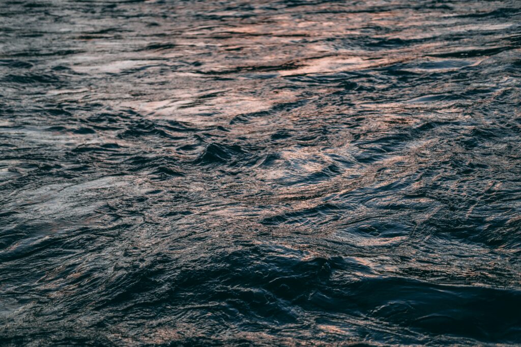 Tranquil water ripples and gentle waves with shimmering sunlight on deep blue textured surface Wallpaper