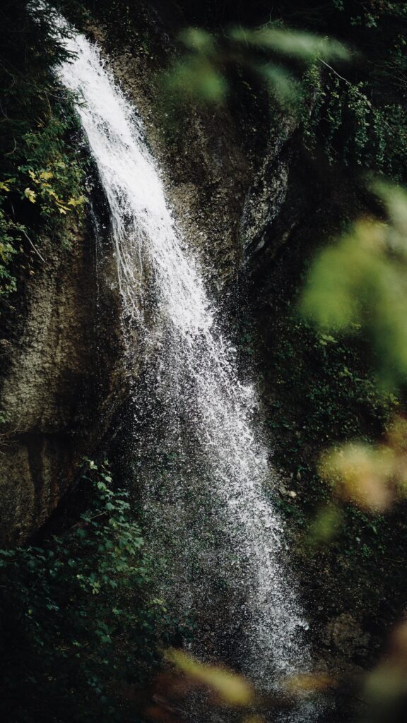 Slender waterfall cascading over mossy rocks and lush green foliage in tranquil forest wallpaper