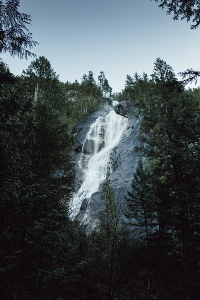 Waterfall cascading over smooth rocks surrounded by dense green forest lush natural landscape background Wallpaper