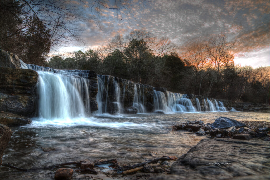 Waterfall cascading over rocks with leafless trees under colorful dusk sky serene landscape wallpaper