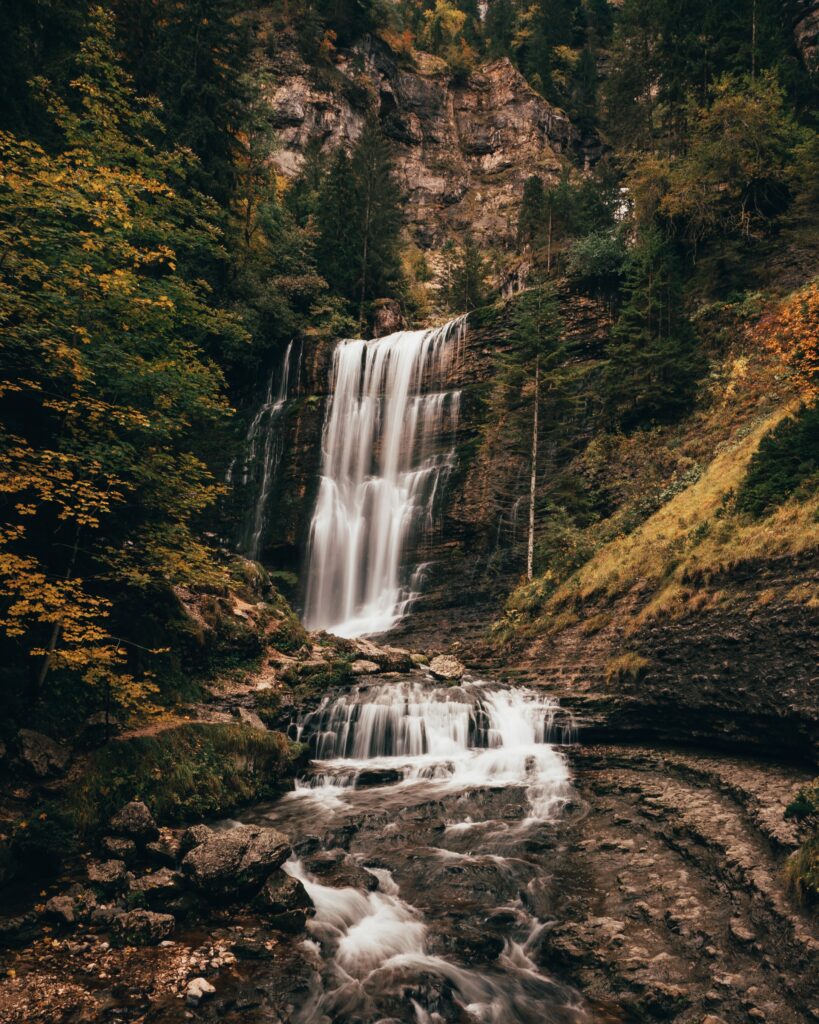 Cascading waterfall over rocks surrounded by lush green forest nature landscape wallpaper background