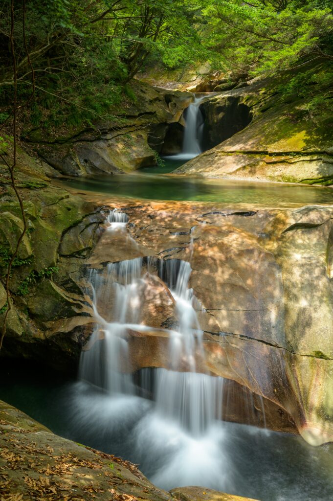 Serene waterfall cascading over rocks surrounded by lush green trees with sunlight filtering through Wallpaper