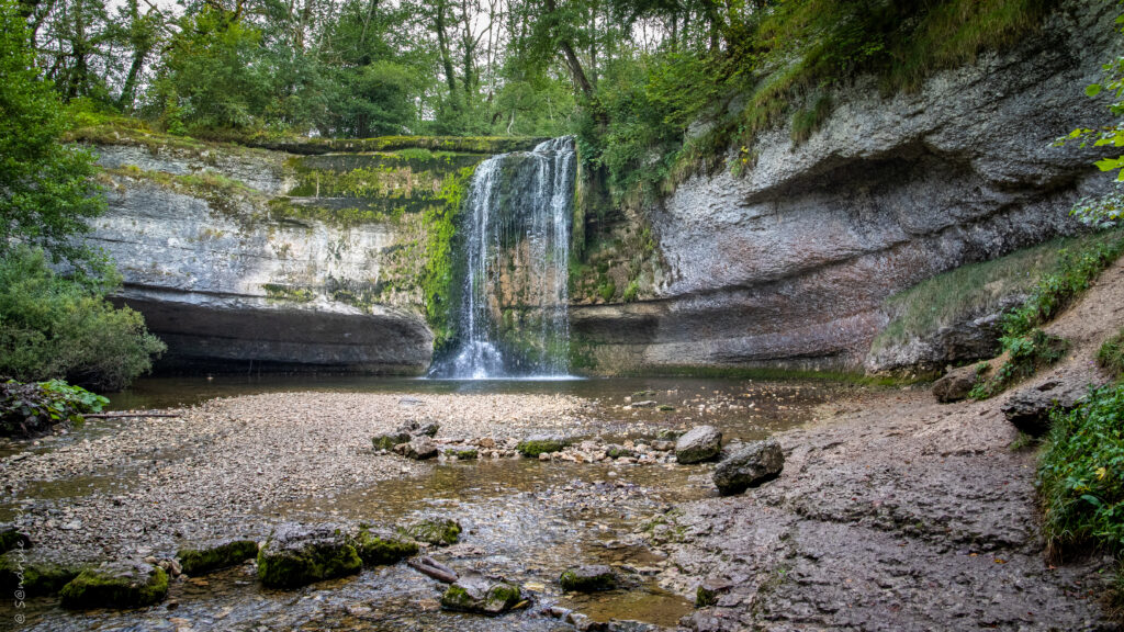 Tranquil waterfall cascading over rocks with lush greenery and misty air in serene nature scene Wallpaper