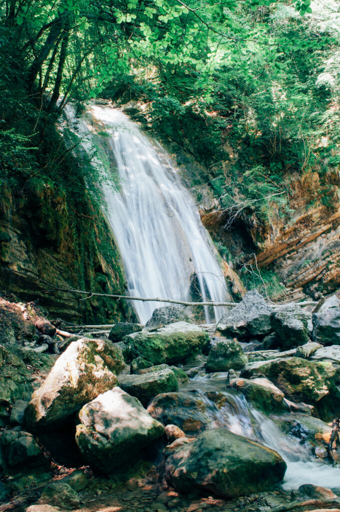 Serene waterfall cascading over rocks surrounded by lush green foliage and sunlight wallpaper