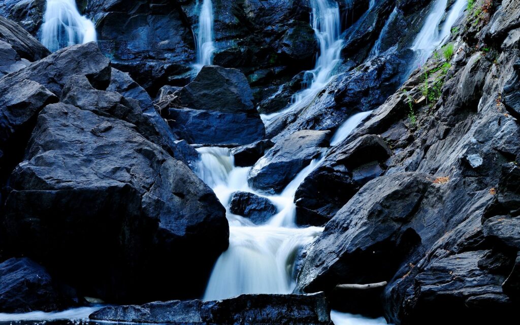 Serene waterfall cascading over dark rocks creating a tranquil blue stream nature wallpaper background