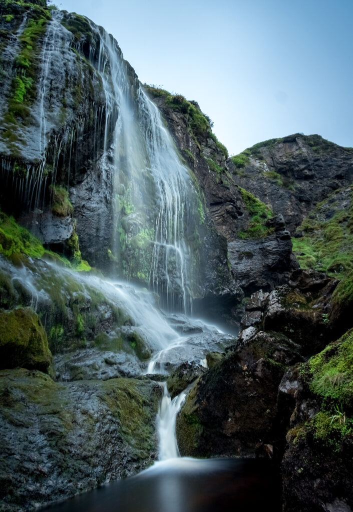 Serene waterfall cascading over rugged rocks with lush green moss and cool blue tones wallpaper