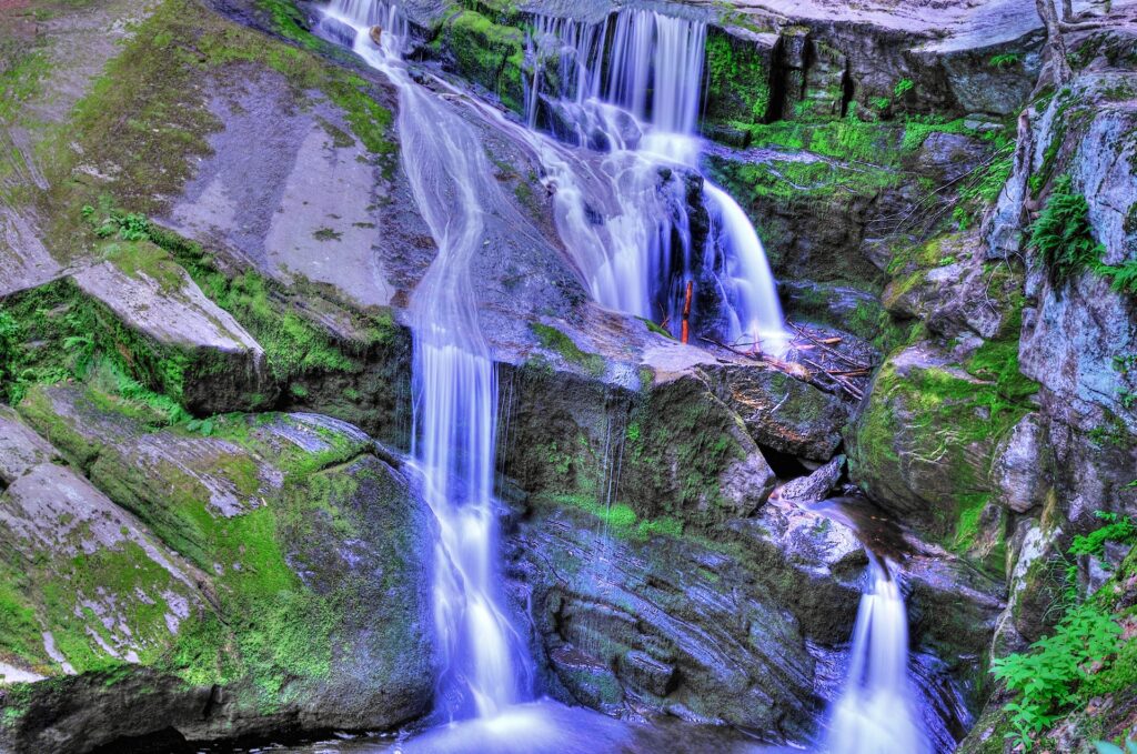Vibrant waterfall cascading over mossy rocks with lush green foliage in a serene natural scene Wallpaper