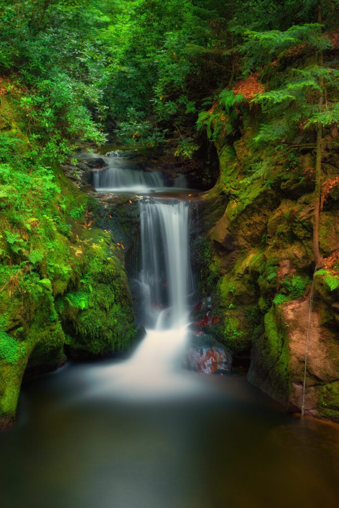 Tranquil waterfall cascading over mossy rocks in a lush green forest high detail wallpaper