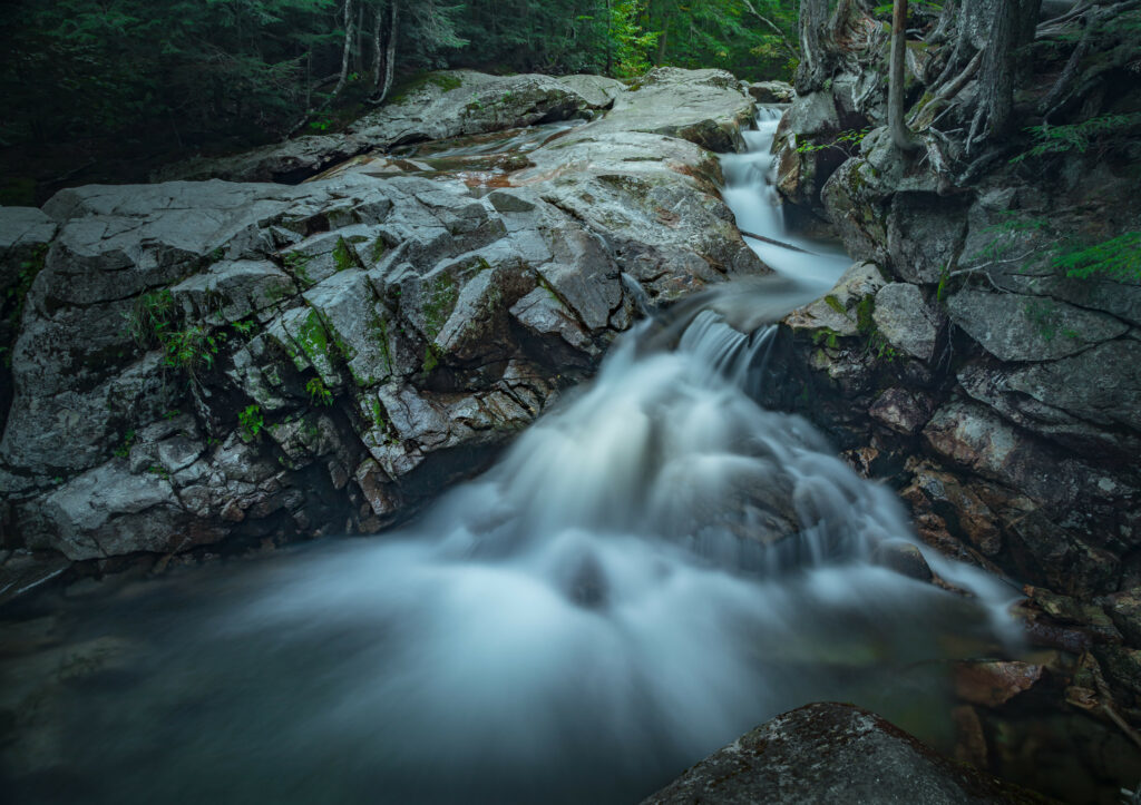 Serene waterfall cascading over mossy rocks in lush green forest with soft water blur effect Wallpaper