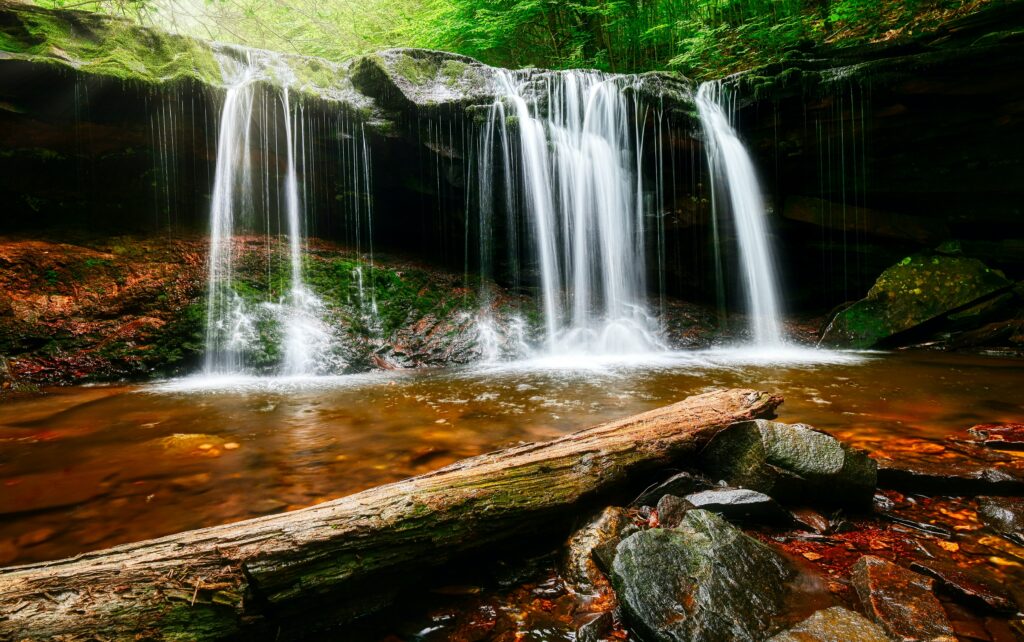 Tranquil waterfall over mossy rocks into clear pool surrounded by lush greenery and smooth stones Wallpaper