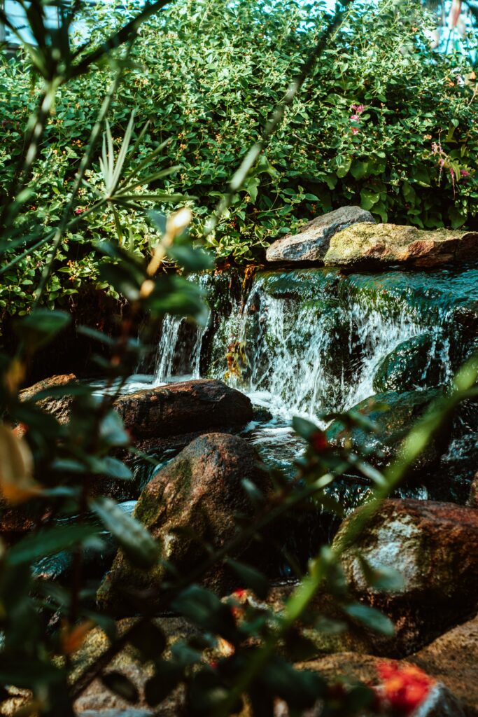 Serene waterfall cascading over mossy stones into clear river with lush green foliage wallpaper