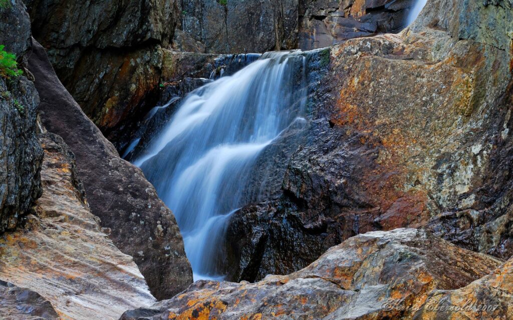 Serene waterfall cascading over colorful rugged rocks with natural textures and earthy tones wallpaper