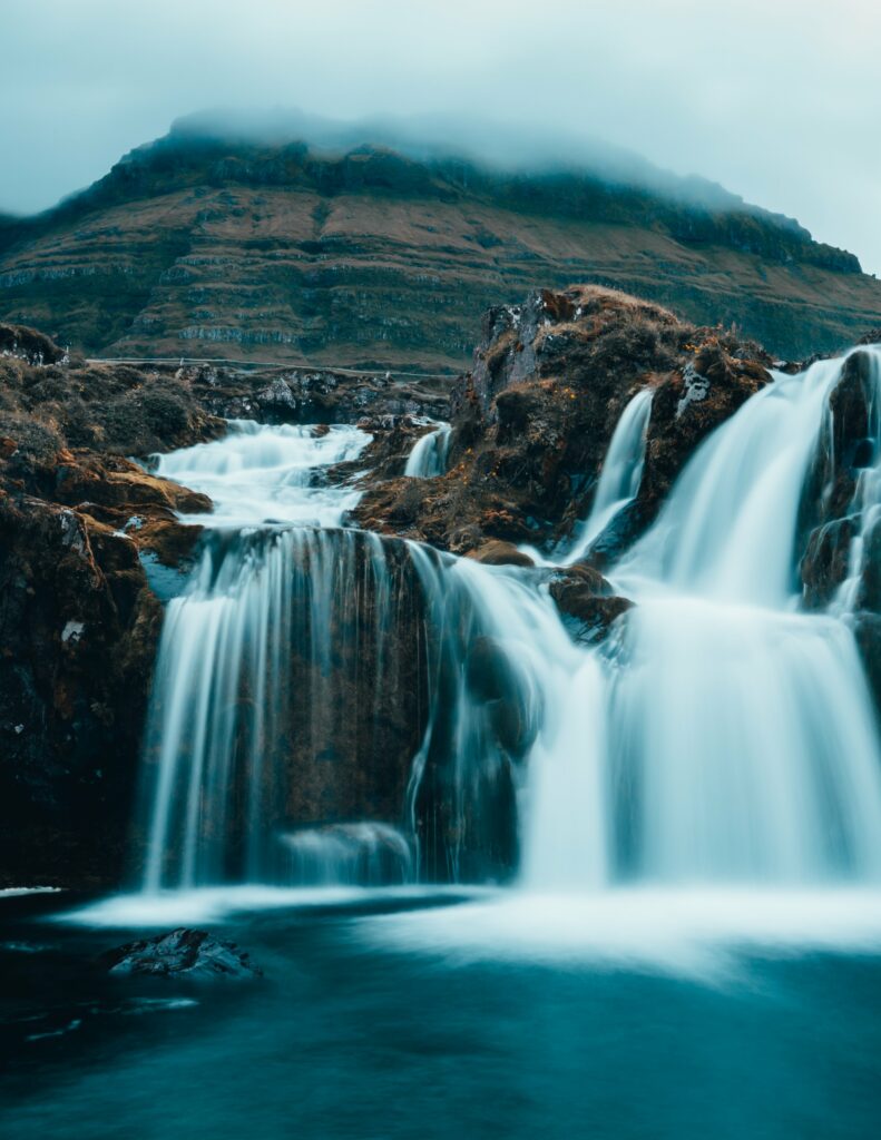 Powerful waterfall over rugged rocks with misty foggy hills in tranquil blue earthy tones wallpaper