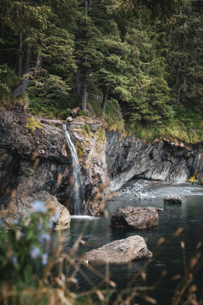 Tranquil waterfall flowing over rocky cliffs into river surrounded by lush green forest trees Wallpaper