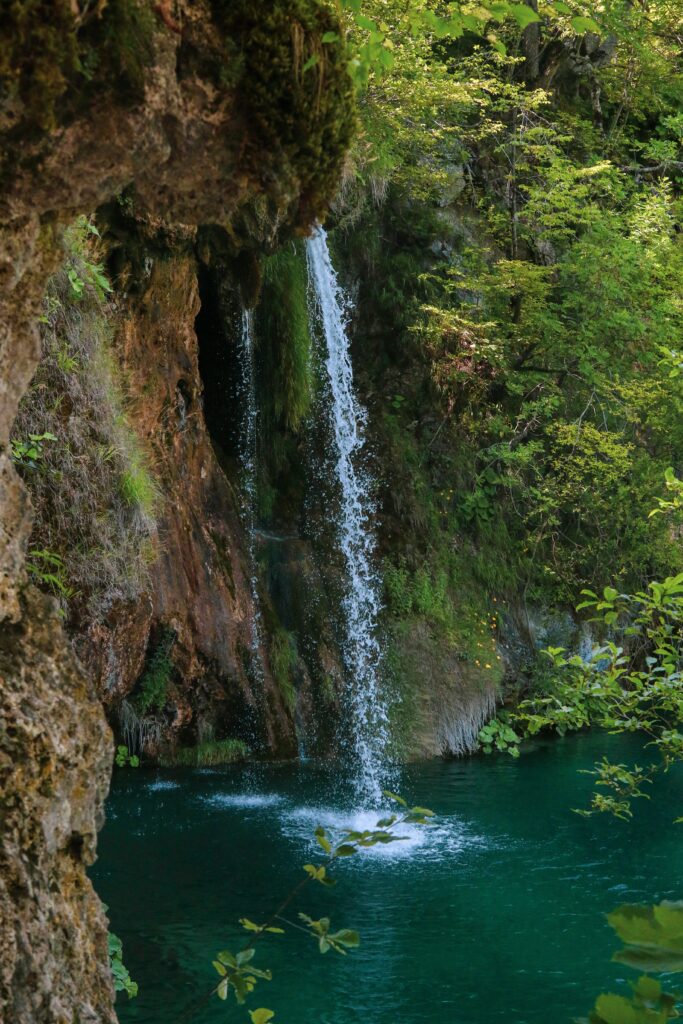Slender waterfall over rocks into turquoise pool with lush greenery and misty spray wallpaper