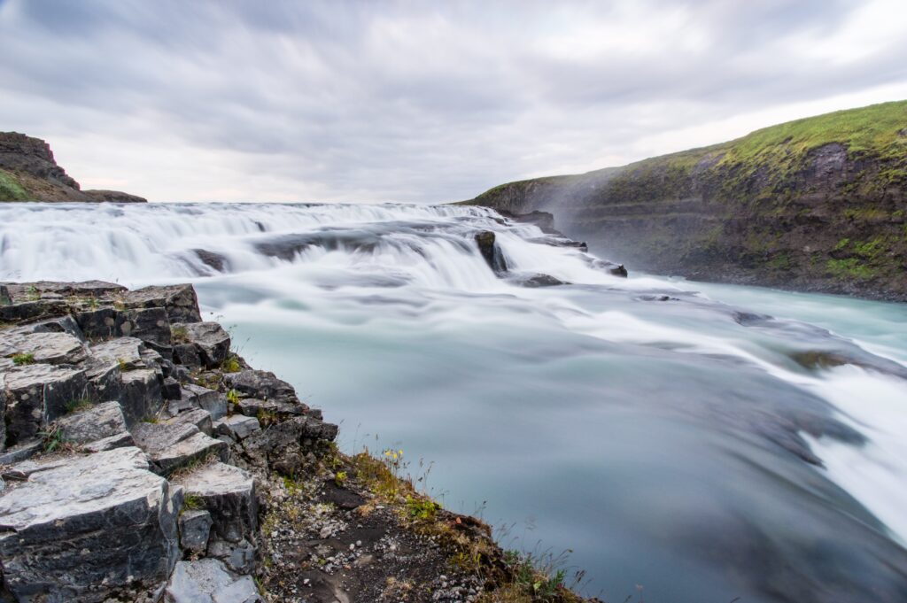 Waterfall cascading over rocks with clear stream under dramatic cloudy sky natural landscape wallpaper