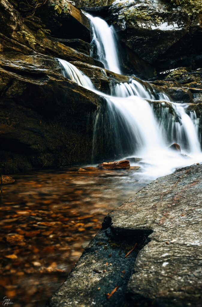 Tranquil waterfall over rugged rocks with clear water flowing into a serene natural pool background Wallpaper