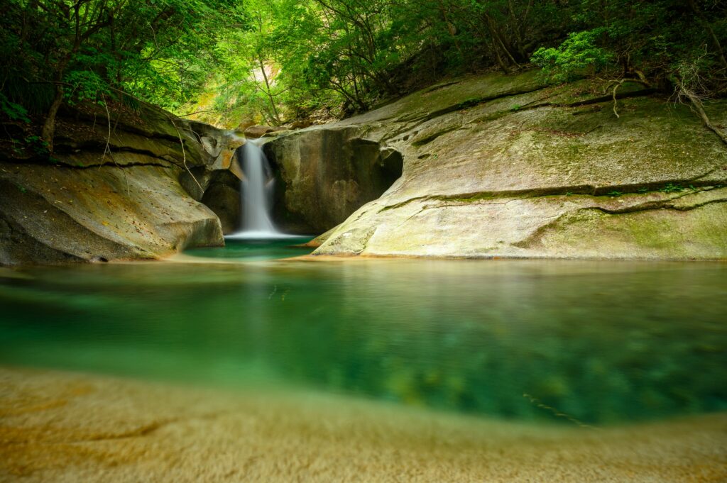 Tranquil waterfall flowing over smooth stone cliffs into clear pool surrounded by lush forest Wallpaper