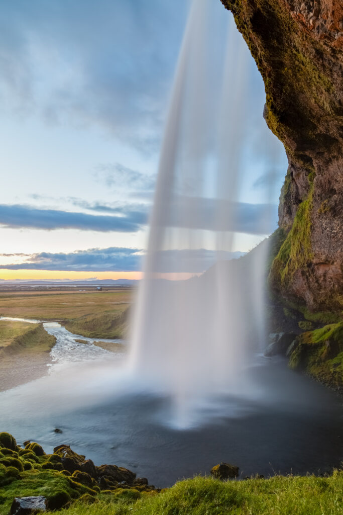 Waterfall cascading into river at sunset with lush moss and open field tranquil nature scene Wallpaper
