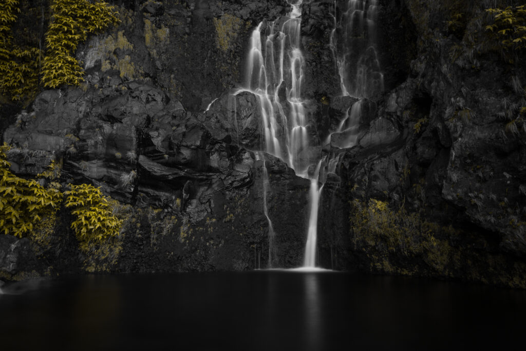 Serene waterfall cascading dark cliffs with yellow green foliage and calm reflective pool background Wallpaper