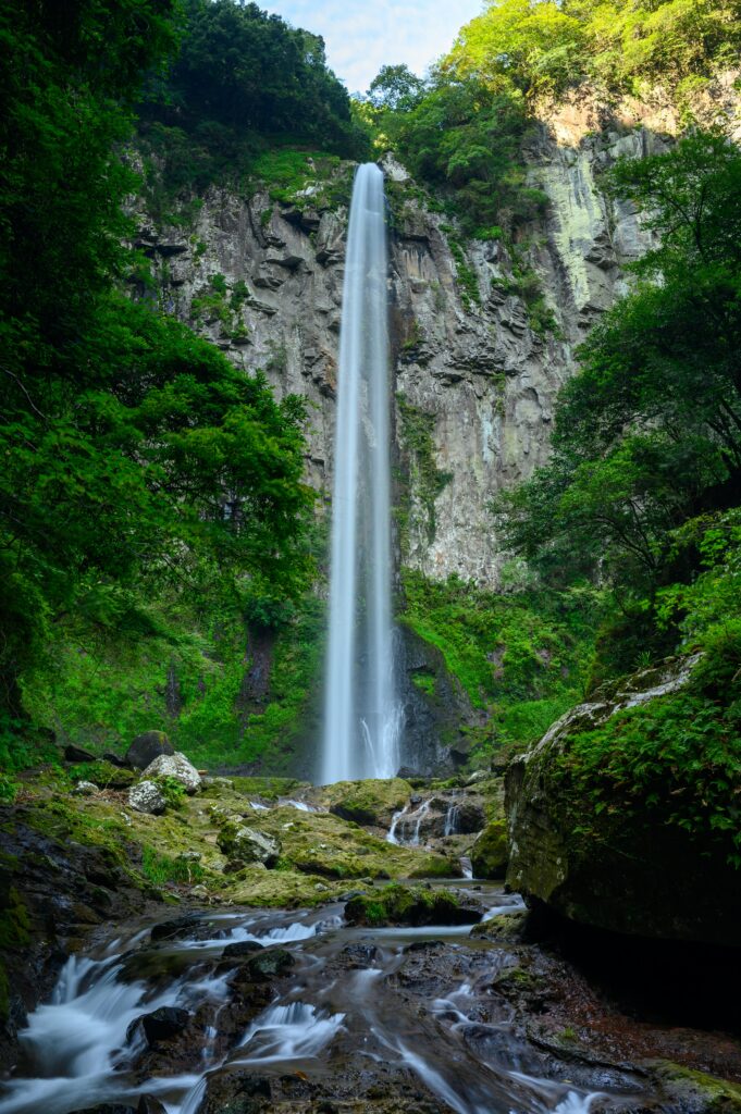 Waterfall cascading down rugged cliff with lush greenery mossy rocks and clear flowing water Wallpaper