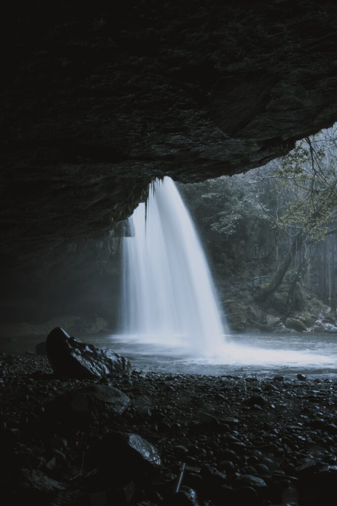 Serene waterfall cascading from rocky cliff into tranquil pool with mist smooth stones wallpaper background