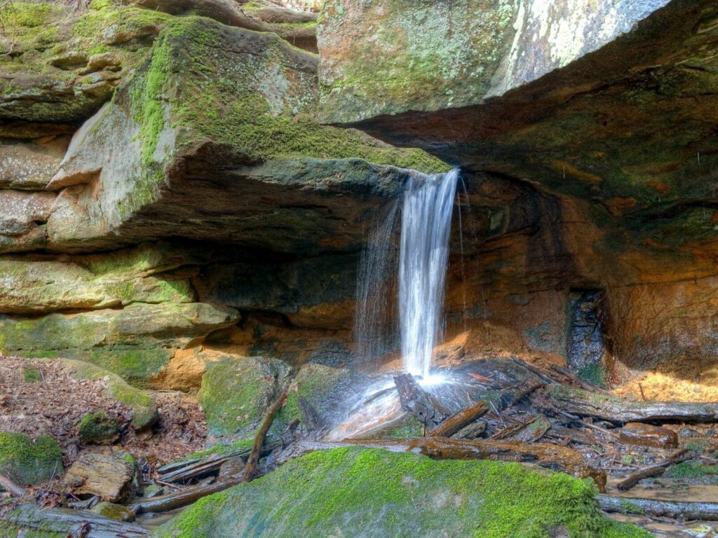 Serene waterfall cascading over rocky ledge with green moss sunlight natural textured wallpaper