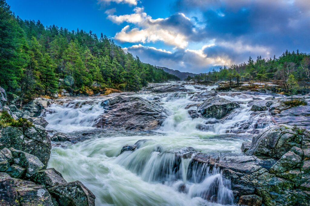 Waterfall cascading over rugged rocks surrounded by lush trees at dusk with dramatic clouds Wallpaper