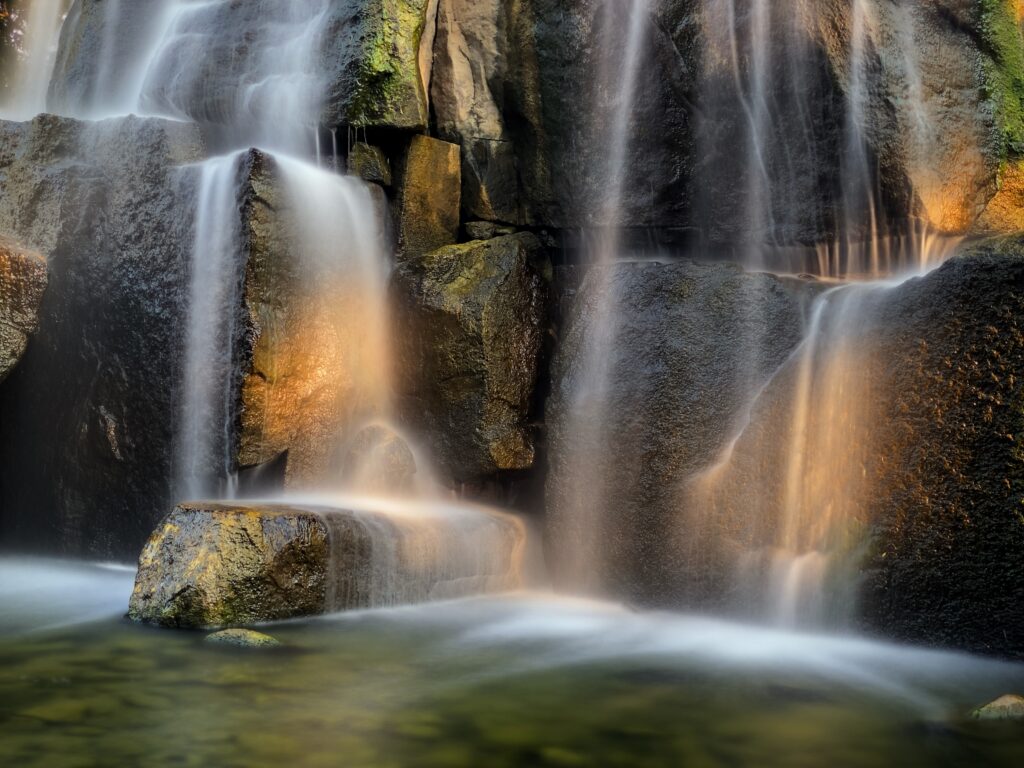 Photorealistic waterfall cascading over smooth rocks with sunlight highlighting vibrant natural textures Wallpaper