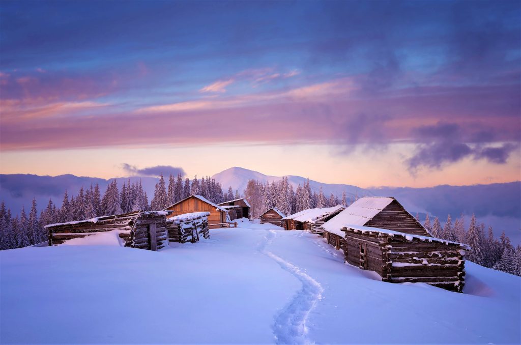 Twilight alpine winter scene with wooden huts snowy pine trees and purple sunset sky background Wallpaper