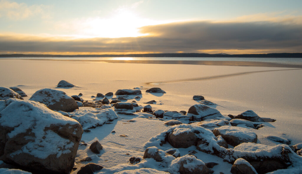 Frozen lake at sunset with snow-covered rocks reflecting warm and cool winter hues wallpaper