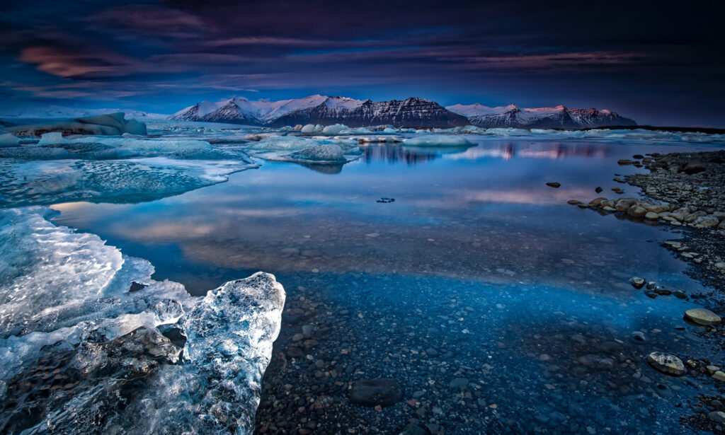 Icy blue mountains reflected in a calm river with snowy peaks and shimmering winter ice wallpaper