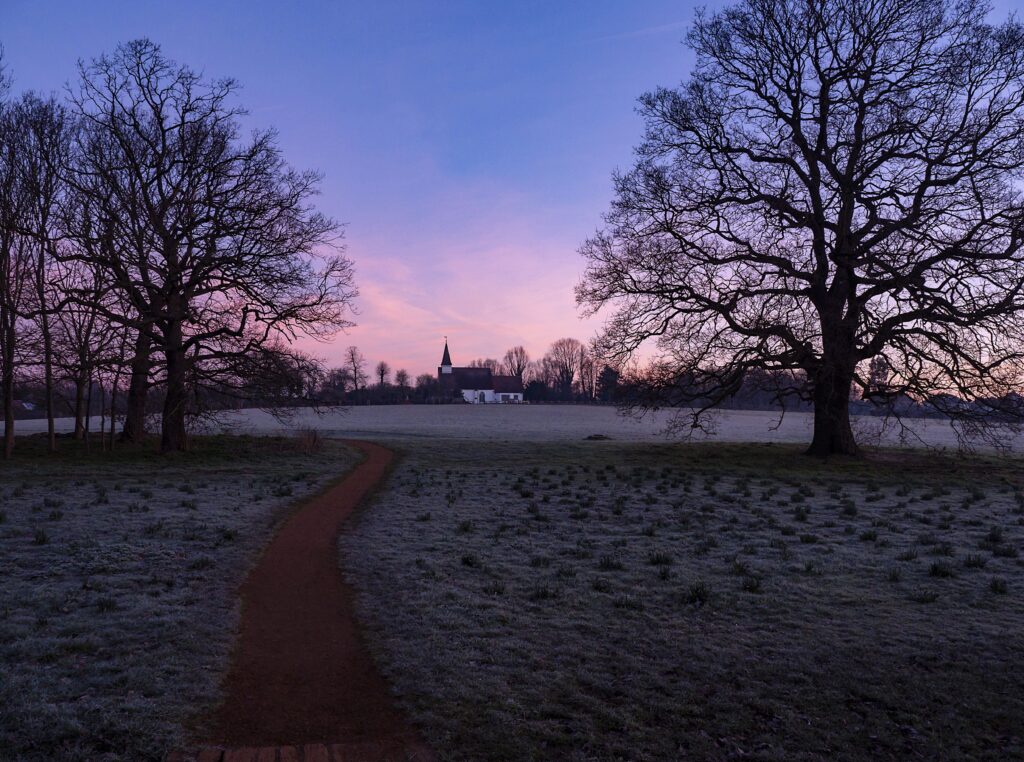 Tranquil sunset wallpaper with distant church frost-covered grass winding path leafless trees