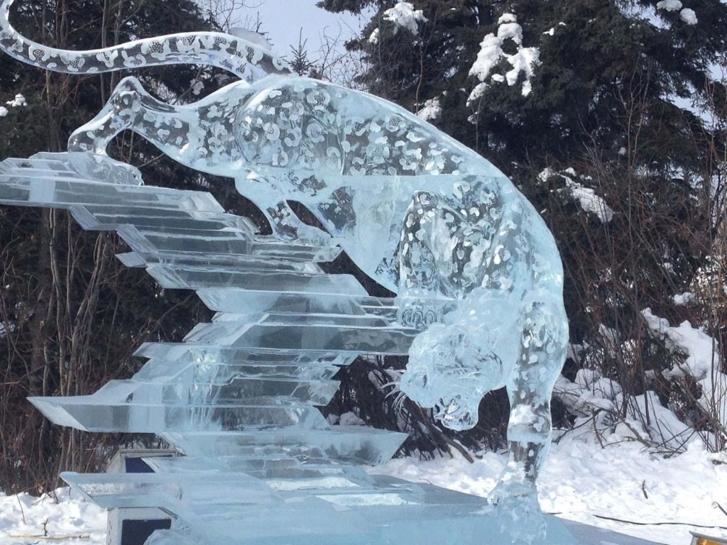 Translucent ice sculpture of a prowling leopard on tiered blocks in snowy forest wallpaper