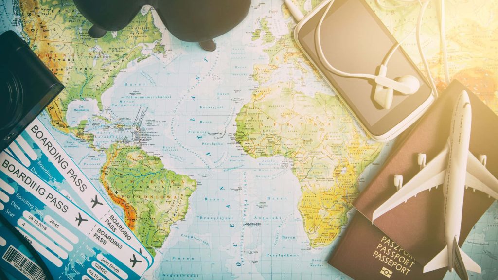 Flat lay travel essentials on world map passport boarding pass camera smartphone earphones sunlight Wallpaper