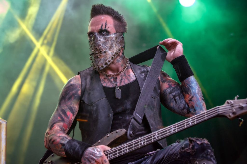 In This Moment bassist Travis Johnson in spiked mask performs live under yellow lights and green haze Wallpaper
