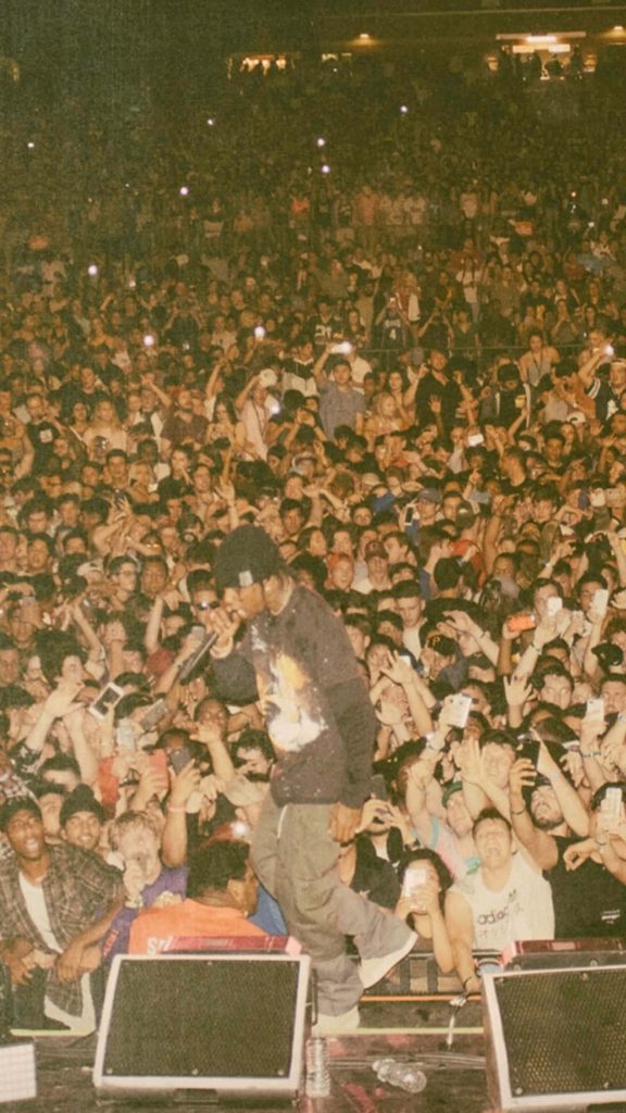 High-angle vintage Travis Scott concert photo with passionate crowd and warm grainy lighting wallpaper