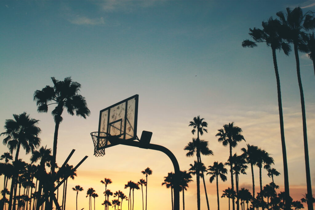 Basketball hoop silhouette framed by palm trees at vibrant colorful sunset in 4K wallpaper