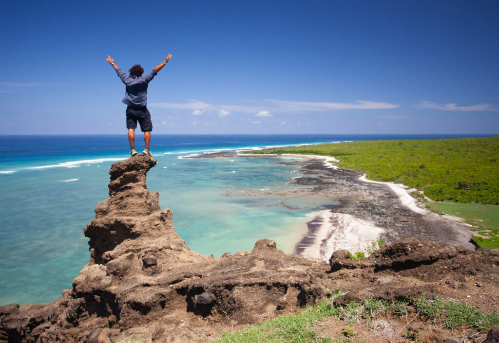Triumphant Man on Rocky Cliff: Adventure Coastal Wallpaper