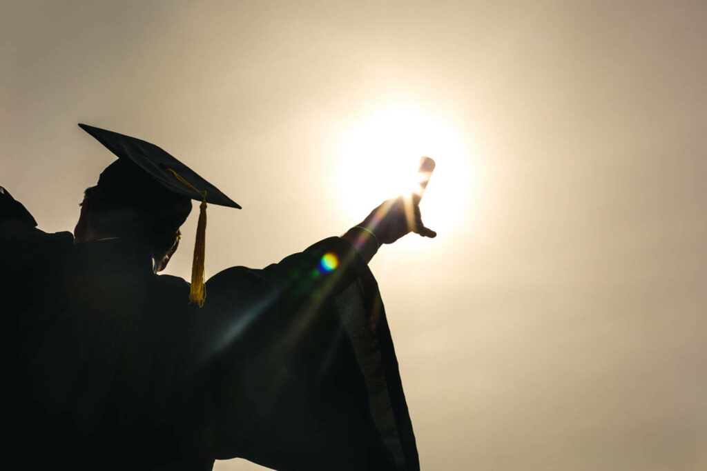 Triumphant Graduate Celebrates Success Against Stunning Graduation Backdrop Wallpaper