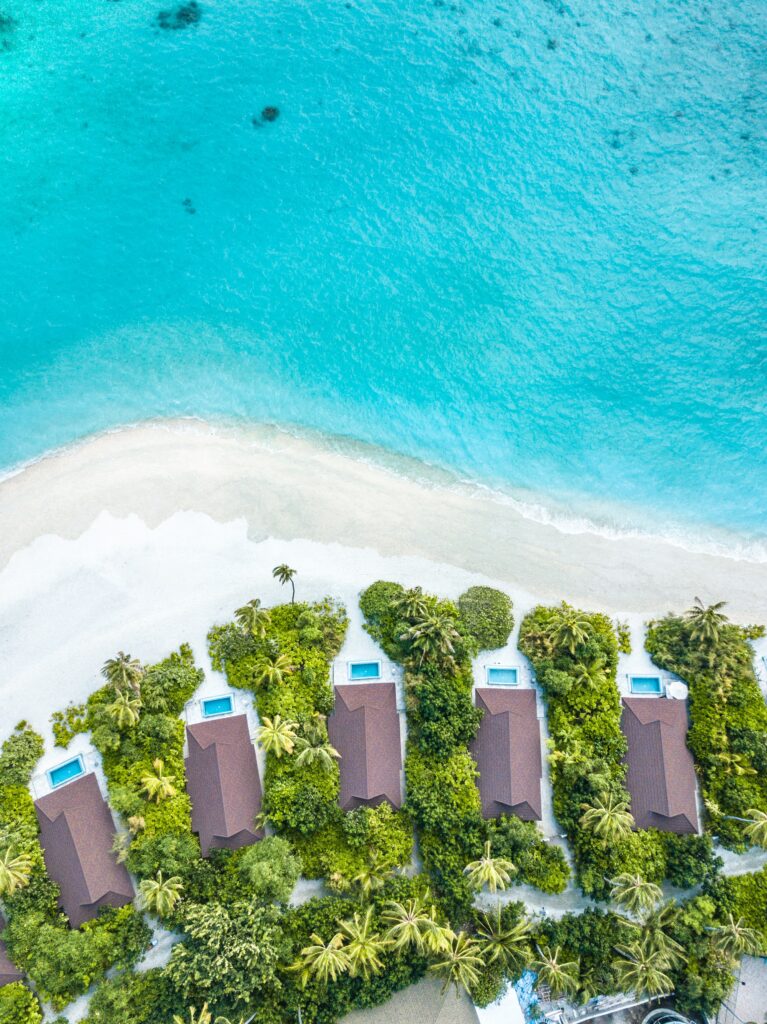 Aerial view of tropical beach with palm trees turquoise sea white sand and beachfront villas Wallpaper