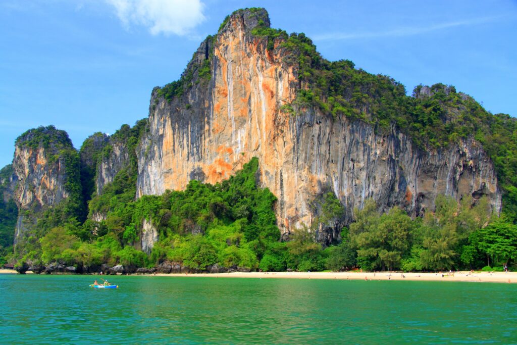 Tropical paradise wallpaper with serene beach emerald water and lush green cliff under blue sky