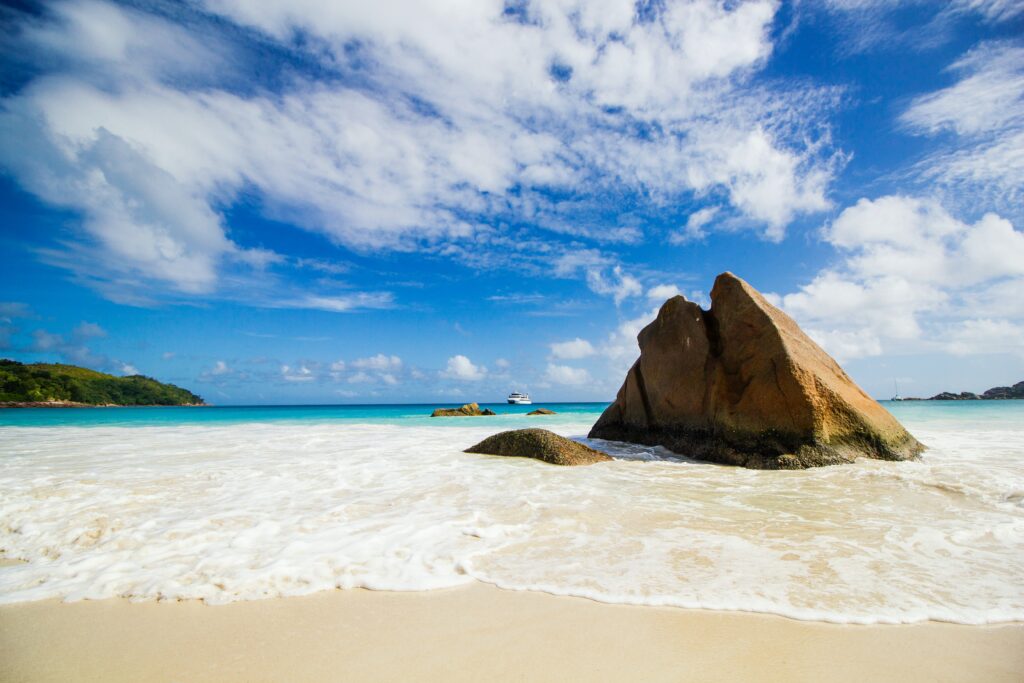 Tropical beach with striking rock formation turquoise sea white sand lush greenery blue sky Wallpaper