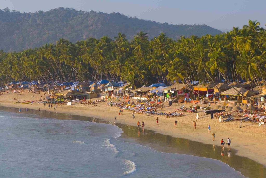 Vibrant Beach Scene: Sunlit Huts, Palm Trees & Happy Beachgoers Wallpaper