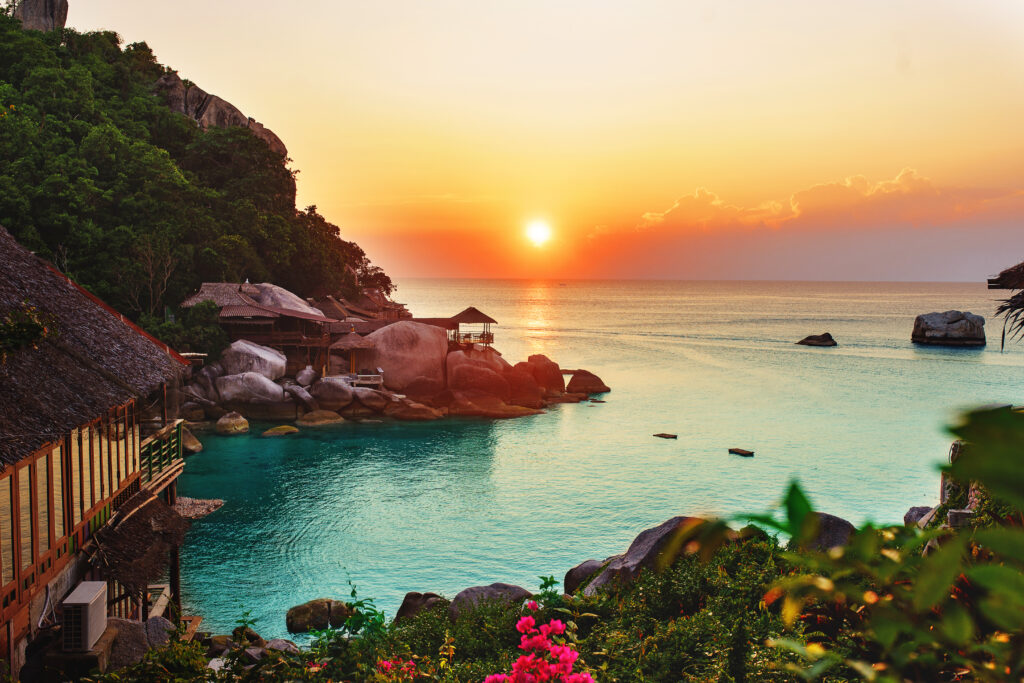 Sunset ocean view wallpaper with turquoise water lush greenery wooden huts and rocky beach