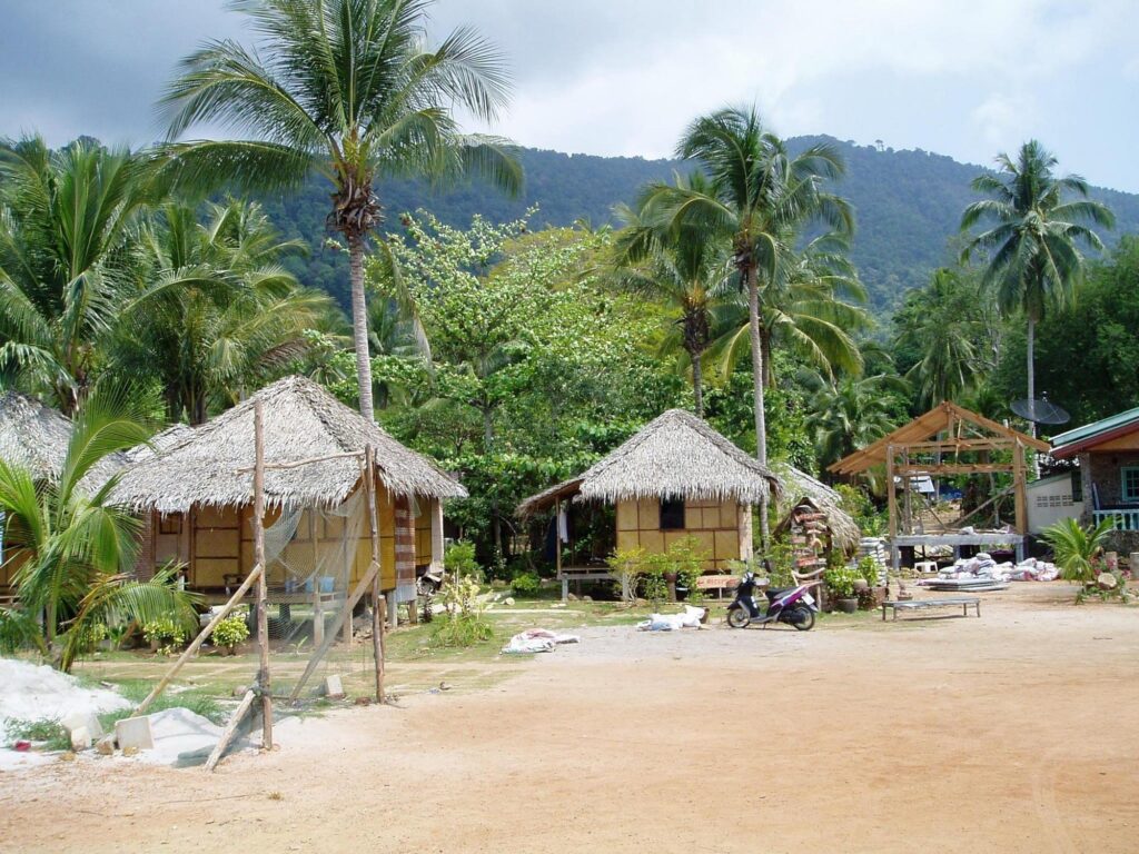 Rustic thatched huts on sandy beach with palm trees moped and green tropical mountains background Wallpaper